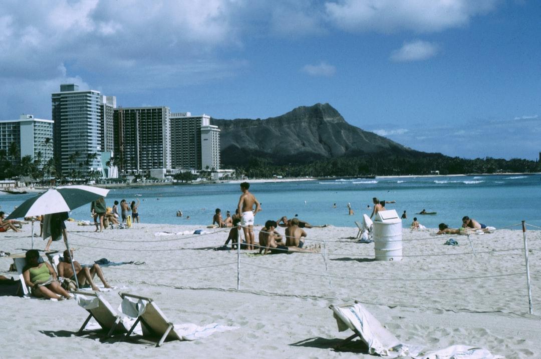 People relax on a sandy beach with ocean and mountains.